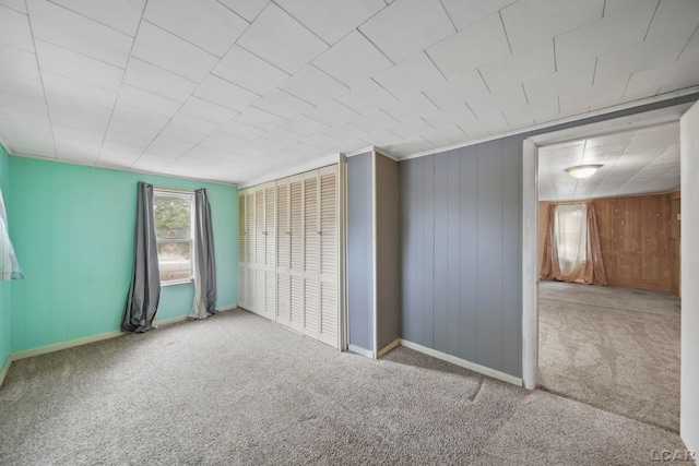 carpeted spare room with wood walls and baseboards