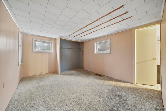 unfurnished bedroom featuring wood walls, carpet, visible vents, and a closet