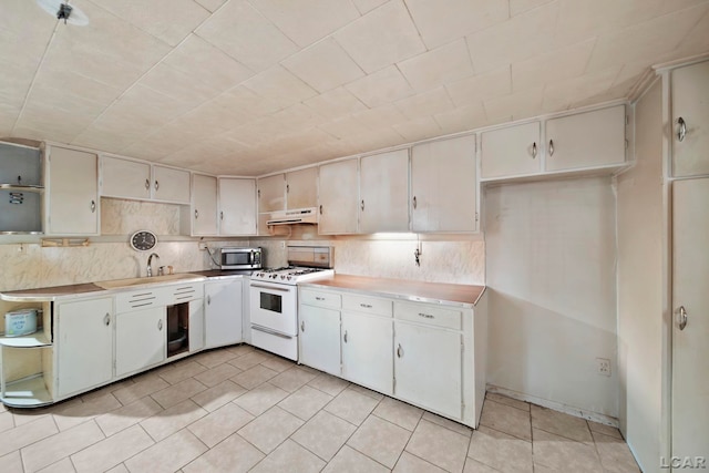 kitchen with stainless steel microwave, white gas range, light countertops, under cabinet range hood, and light tile patterned flooring