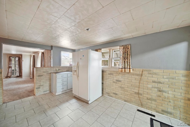 kitchen featuring light tile patterned floors, brick wall, and a wainscoted wall