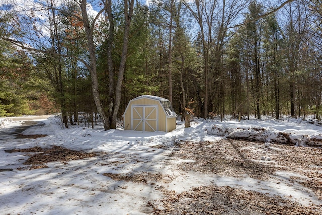 yard layered in snow with an outbuilding, a storage unit, and a view of trees