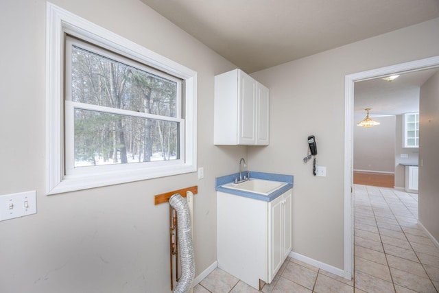 laundry area with light tile patterned floors, cabinet space, baseboards, and a sink