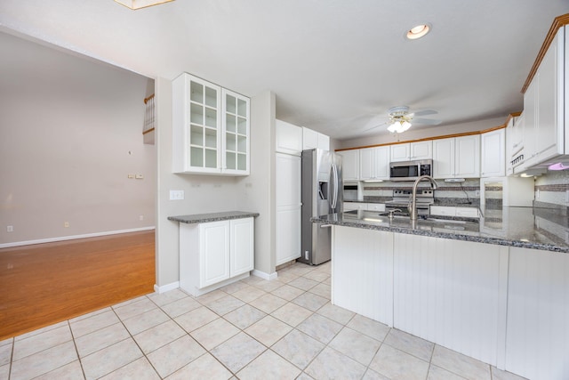 kitchen with light tile patterned flooring, stainless steel appliances, a peninsula, white cabinets, and glass insert cabinets