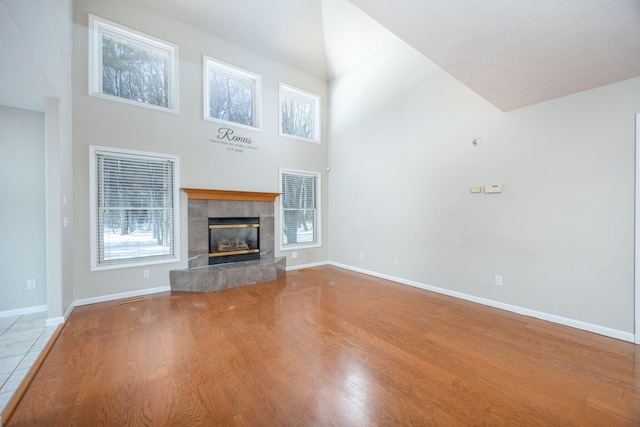 unfurnished living room featuring a towering ceiling, baseboards, wood finished floors, and a tile fireplace