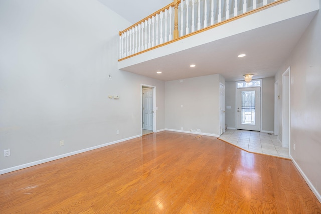 unfurnished living room with wood finished floors, a towering ceiling, and baseboards