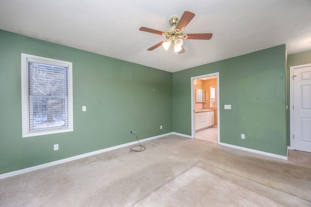 unfurnished bedroom featuring light carpet, ceiling fan, baseboards, and ensuite bathroom