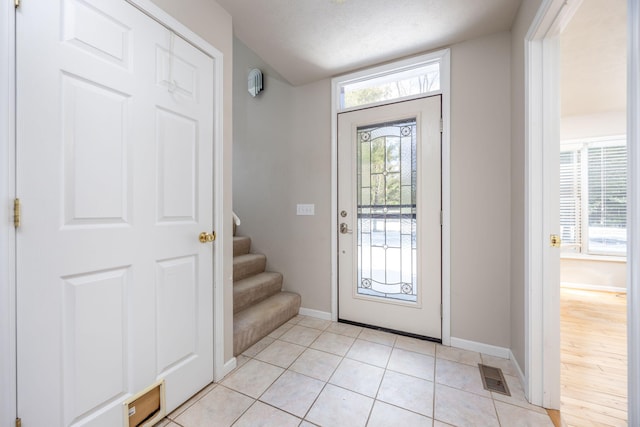 foyer entrance featuring light tile patterned floors, visible vents, a textured ceiling, baseboards, and stairs