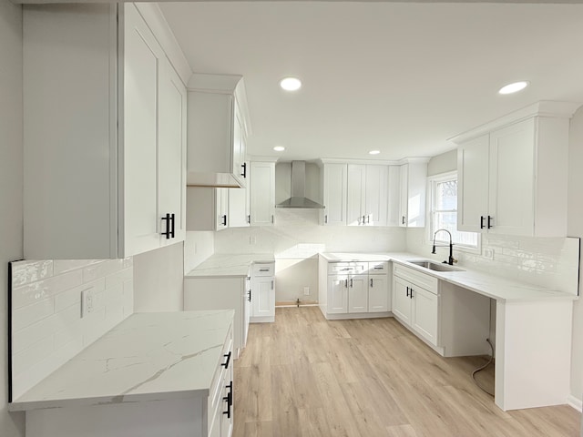 kitchen with wall chimney exhaust hood, light wood-type flooring, a sink, and decorative backsplash