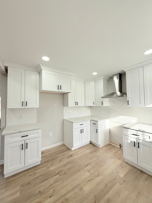 kitchen featuring light wood-style floors, white cabinetry, wall chimney range hood, and decorative backsplash