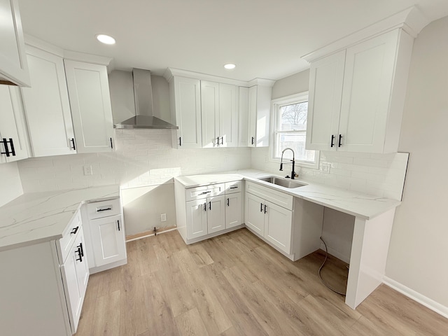 kitchen with light stone counters, decorative backsplash, light wood-style floors, a sink, and wall chimney exhaust hood