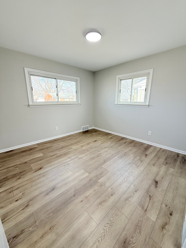 empty room with a healthy amount of sunlight, visible vents, baseboards, and wood finished floors