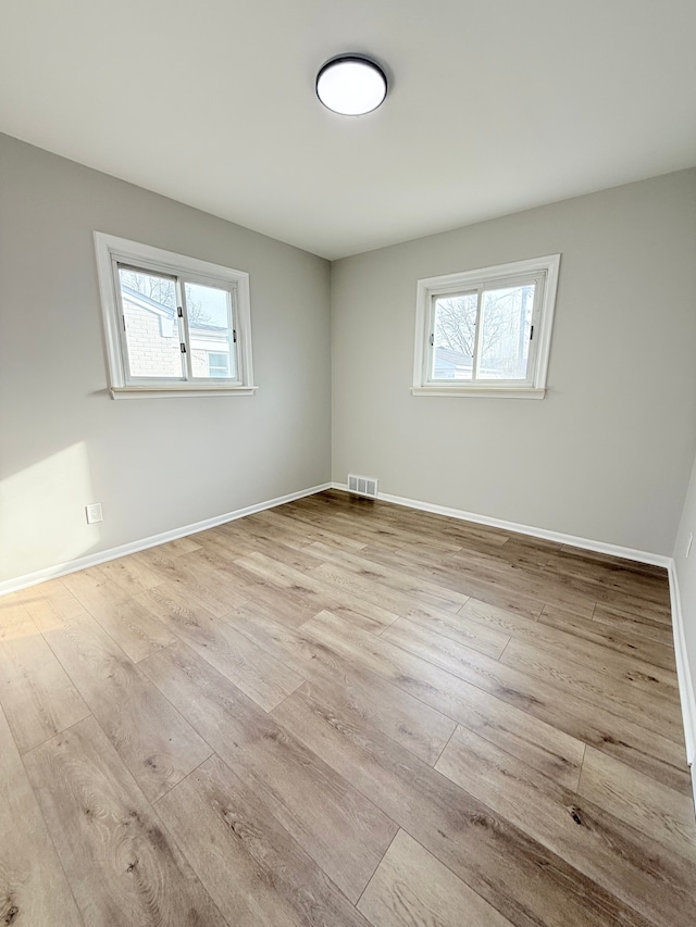 empty room with a healthy amount of sunlight, visible vents, baseboards, and wood finished floors