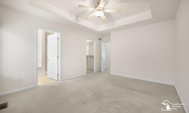 unfurnished bedroom with baseboards, a spacious closet, a tray ceiling, and light colored carpet