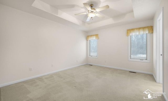 spare room featuring baseboards, a tray ceiling, ceiling fan, and light colored carpet