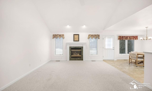 unfurnished living room with lofted ceiling, carpet floors, a fireplace, and a notable chandelier