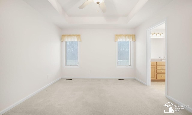 unfurnished bedroom featuring baseboards, a raised ceiling, light colored carpet, ensuite bathroom, and a sink