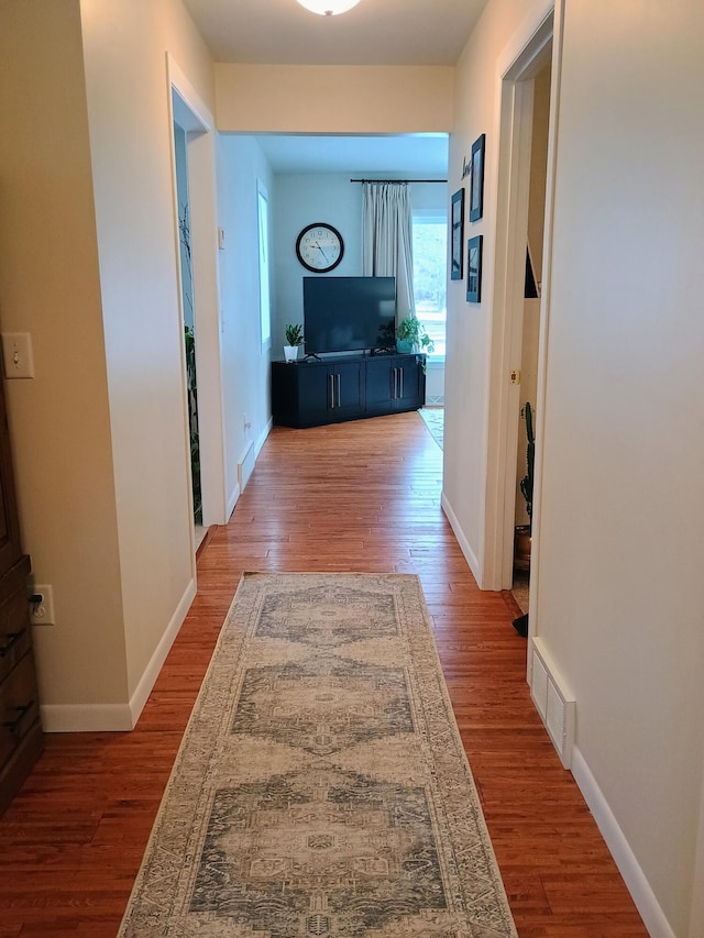 corridor featuring visible vents, baseboards, and wood finished floors