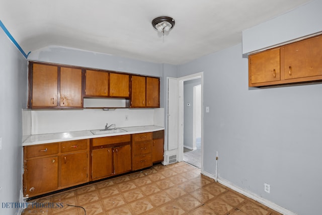 kitchen with a sink, baseboards, light countertops, brown cabinets, and light floors