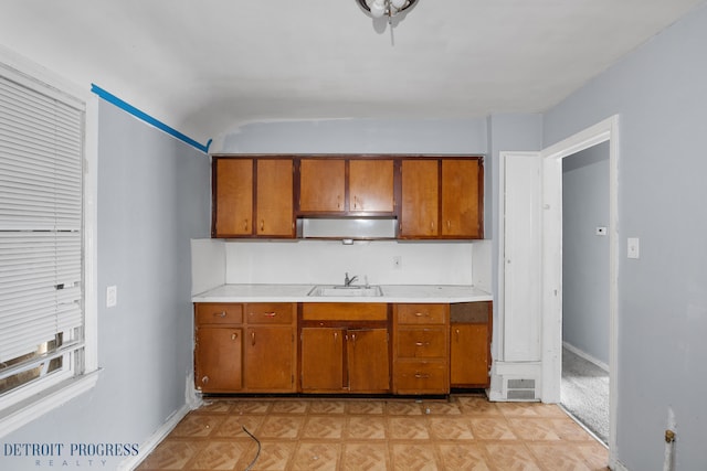 kitchen featuring light countertops, brown cabinetry, a sink, and baseboards