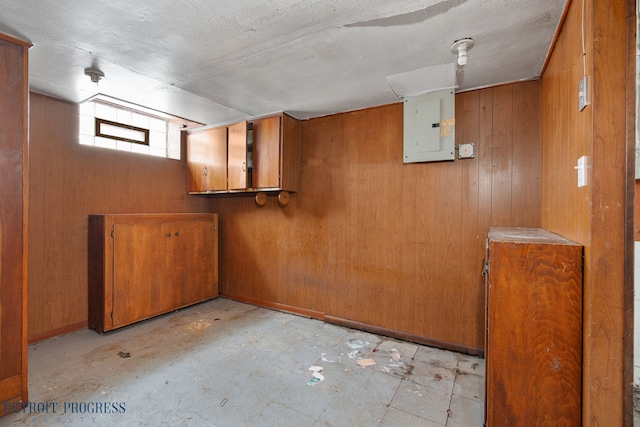 basement featuring electric panel, wooden walls, and baseboards