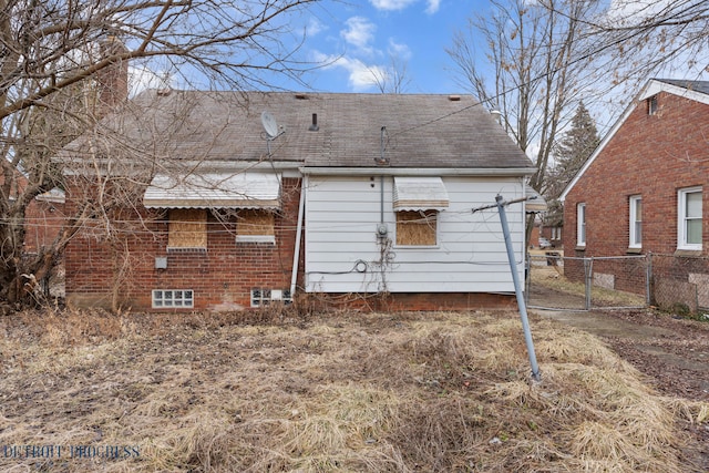 rear view of house featuring brick siding, a shingled roof, fence, and a gate