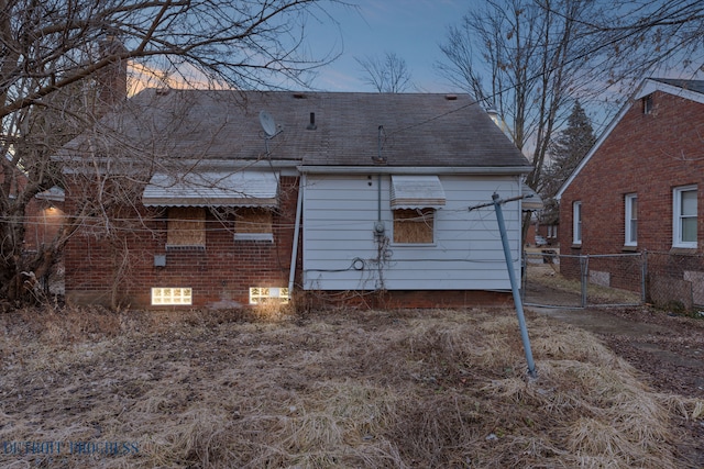 back of property with brick siding, a gate, fence, and roof with shingles