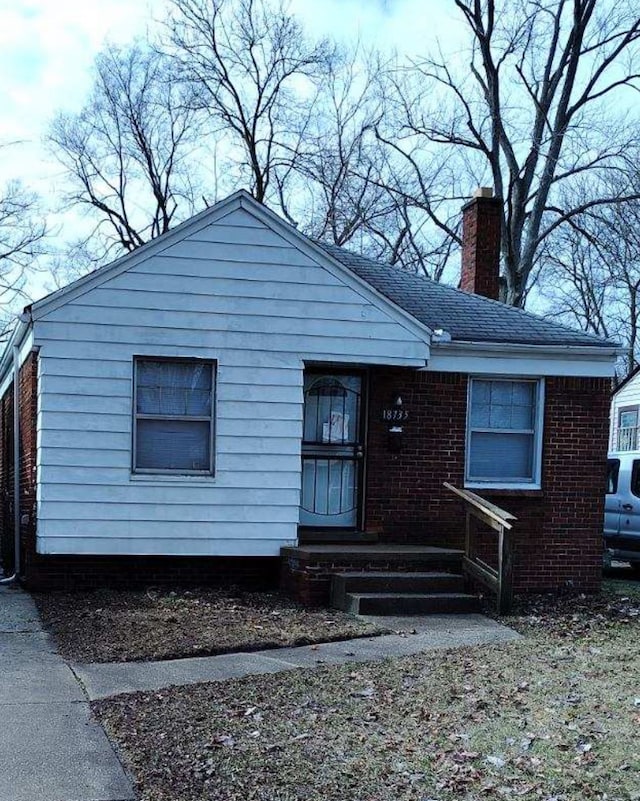 bungalow featuring a shingled roof, a chimney, and brick siding