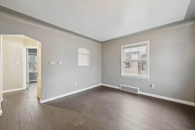 unfurnished room with arched walkways, dark wood-style flooring, visible vents, and baseboards