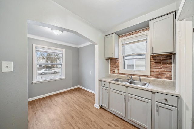 kitchen with light wood-style flooring, a sink, a healthy amount of sunlight, baseboards, and backsplash