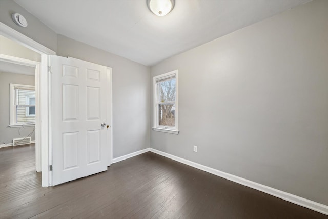 unfurnished room with visible vents, dark wood finished floors, and baseboards