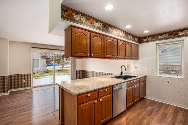 kitchen with a wainscoted wall, stainless steel dishwasher, a sink, and dark wood finished floors