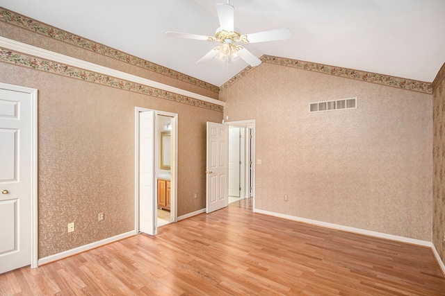 interior space with wallpapered walls, baseboards, visible vents, lofted ceiling, and light wood-style floors