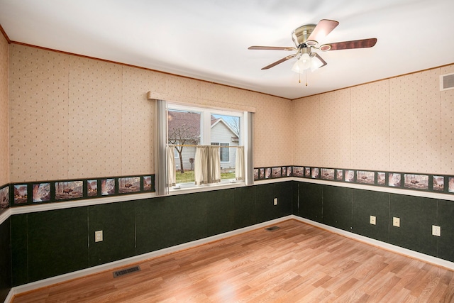 spare room featuring wood finished floors, wainscoting, visible vents, and wallpapered walls