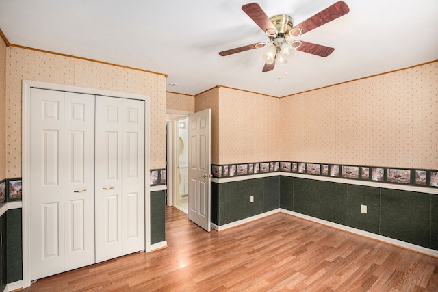 unfurnished bedroom with ornamental molding, wainscoting, light wood finished floors, and wallpapered walls