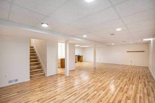 finished below grade area featuring stairway, light wood-style flooring, visible vents, and baseboards