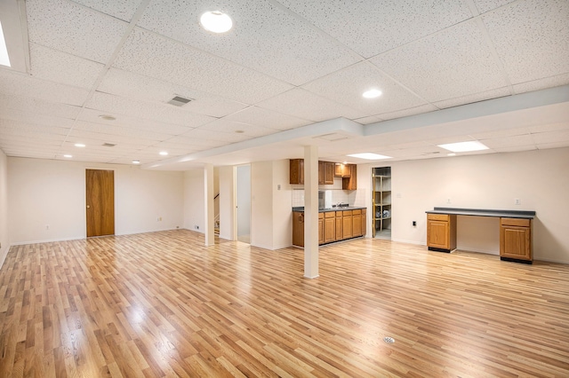 finished basement with light wood-type flooring, a paneled ceiling, and baseboards