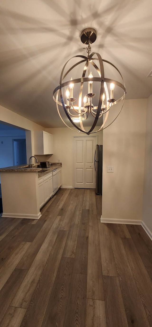 unfurnished dining area featuring baseboards, dark wood finished floors, and a notable chandelier