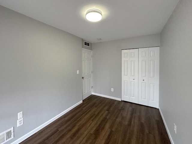 unfurnished bedroom with dark wood-style floors, a closet, visible vents, and baseboards