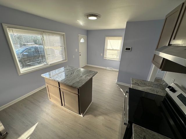 kitchen with visible vents, baseboards, light wood-style flooring, a kitchen island, and light stone countertops