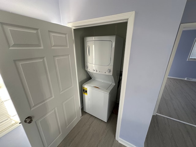 laundry area with stacked washer and dryer, wood finished floors, and laundry area