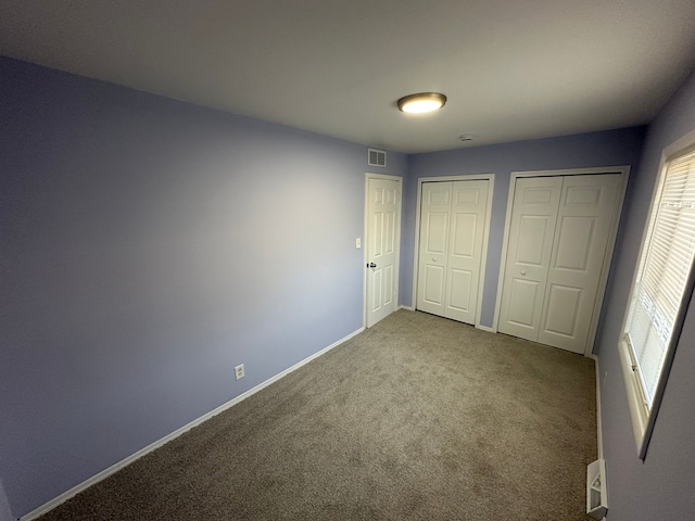 unfurnished bedroom featuring baseboards, visible vents, multiple closets, and carpet flooring