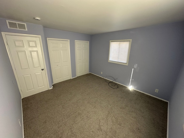 unfurnished bedroom with carpet floors, visible vents, and multiple closets