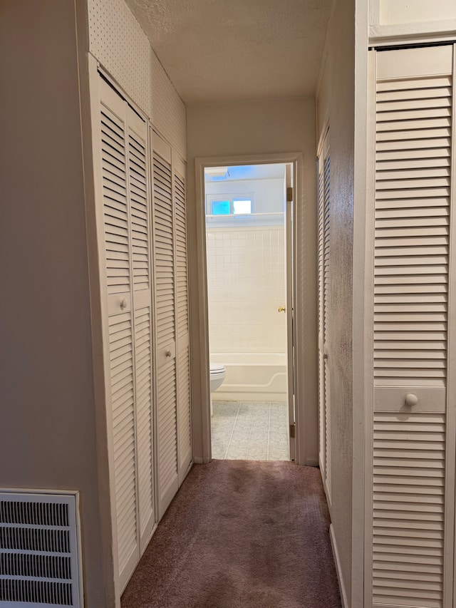 hallway with visible vents, a textured ceiling, and carpet flooring