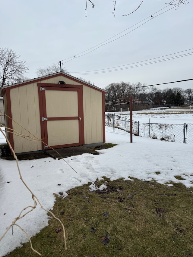 snow covered structure with a storage shed, fence, and an outbuilding