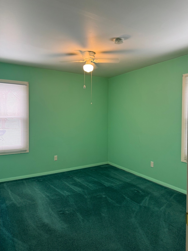 spare room with baseboards, dark carpet, and a ceiling fan