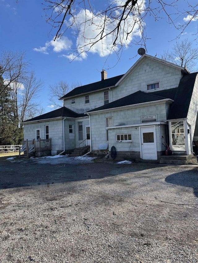 back of house with gravel driveway and a chimney
