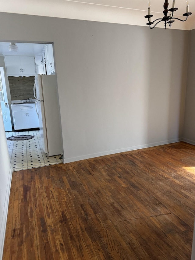 unfurnished room with a chandelier, dark wood finished floors, and baseboards