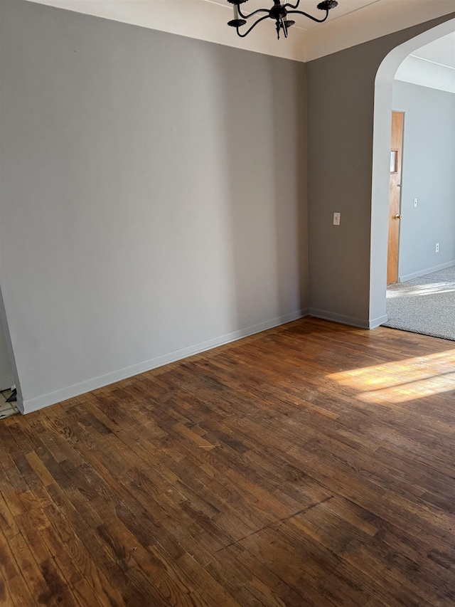 unfurnished room with baseboards, arched walkways, dark wood finished floors, and a notable chandelier