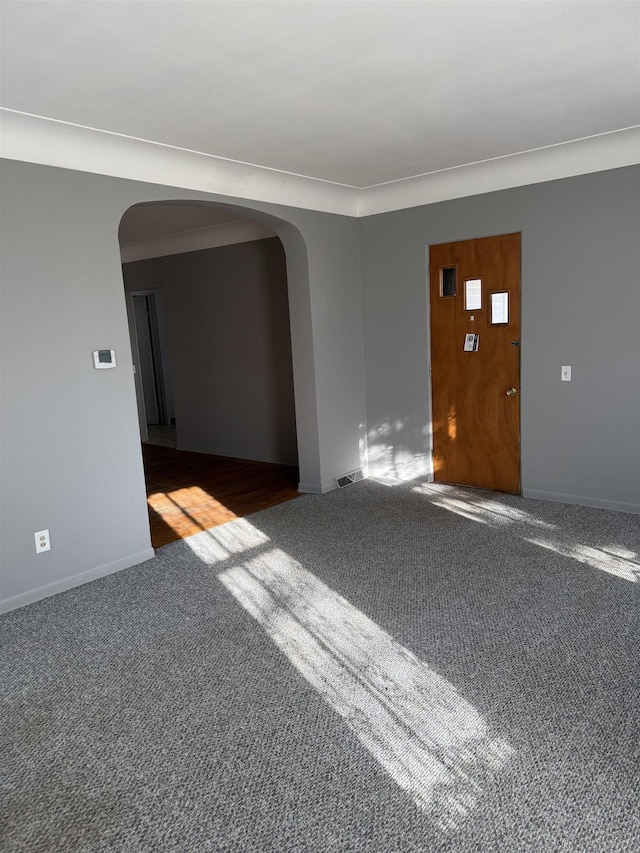 carpeted empty room featuring arched walkways, visible vents, and baseboards