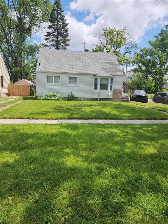 view of front of property with a shingled roof, fence, and a front yard